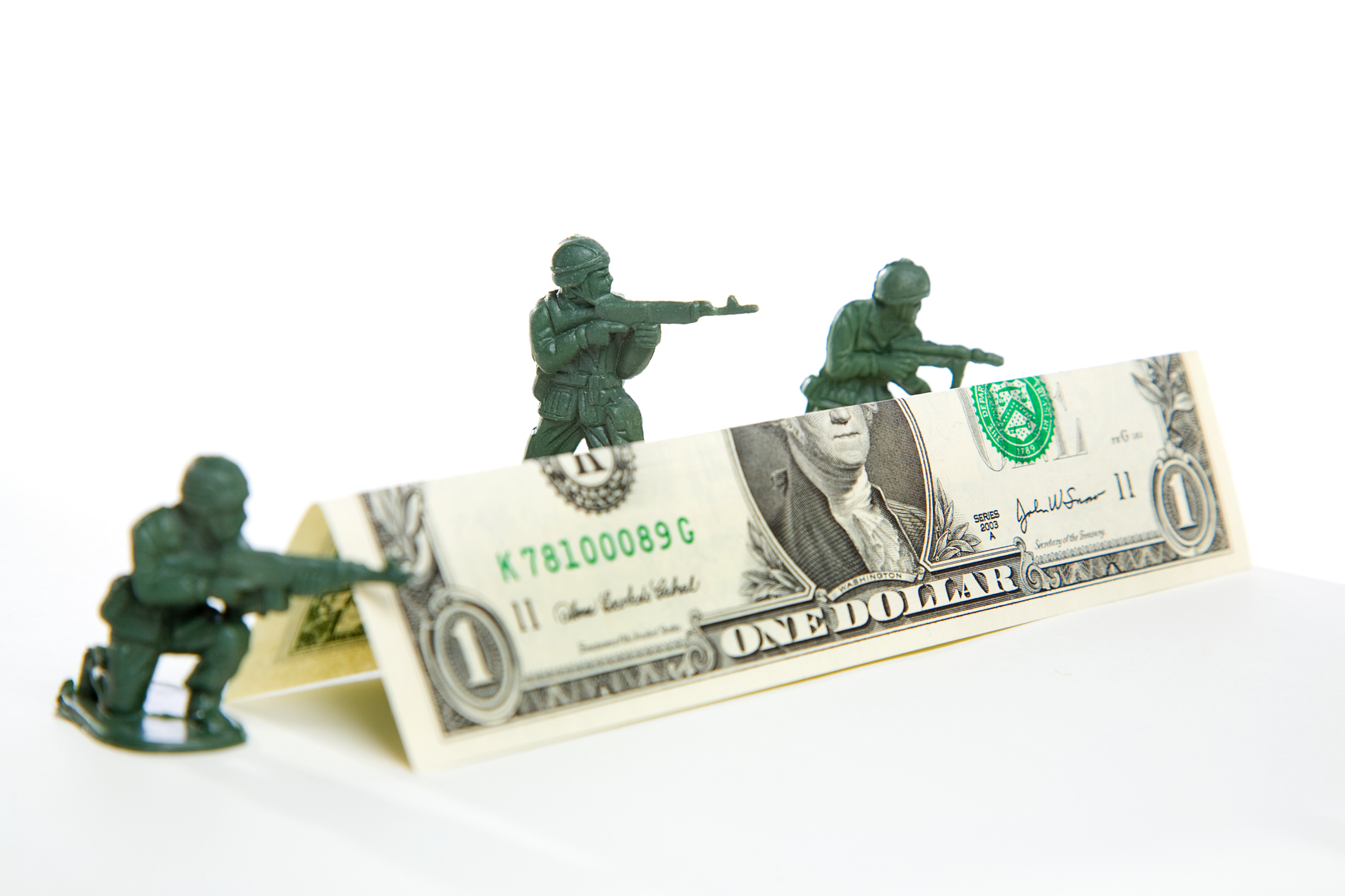 Drei Plastikspielzeugsoldaten schießen über eine Barrikade aus einem gefalteten Dollarschein