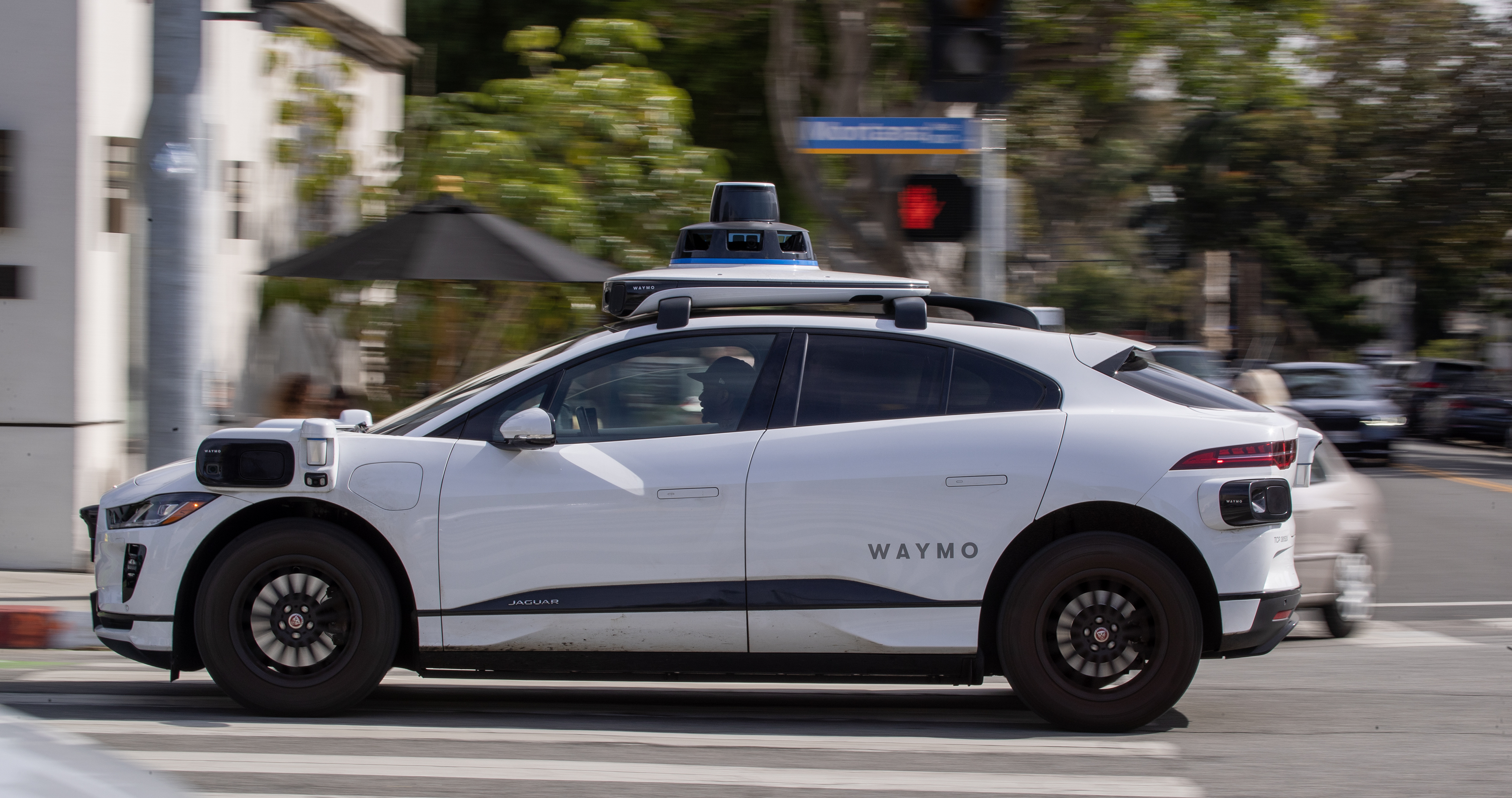Ein autonomes Waymo-Fahrzeug, das auf einer von Bäumen gesäumten Straße in Santa Monica unterwegs ist.