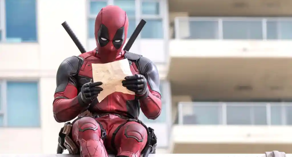 Deadpool schaut auf ein Stück Papier, während er in Deadpool auf der Kante eines Gebäudes sitzt