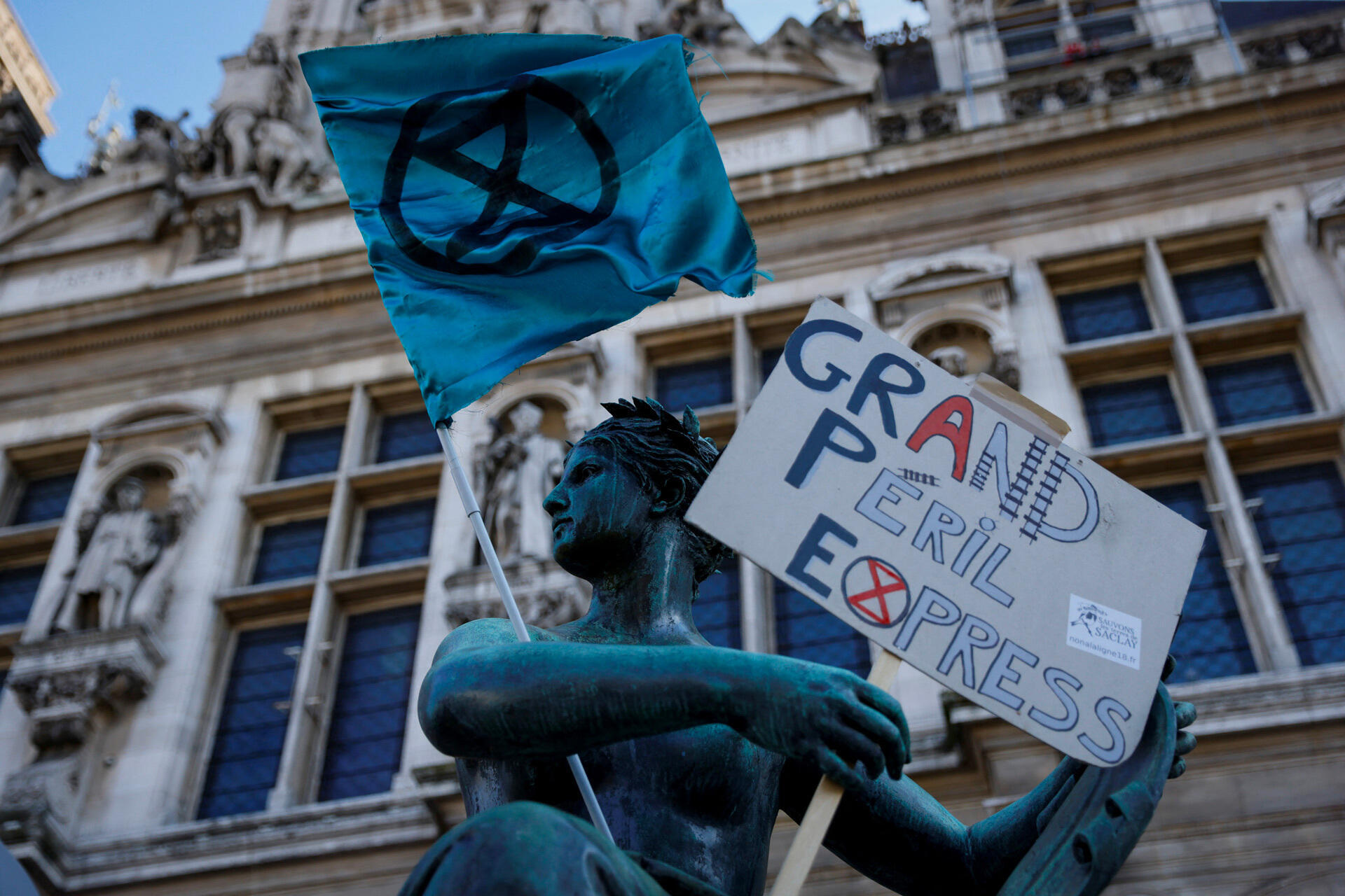 A sign on a statue reads 'Grand Péril Express' next to a flag of the Extinction-Rebellion movement during a demonstration against plans to urbanize agricultural land in Île-de-France, in front of the Hôtel de Ville in Paris, October 10, 2021.