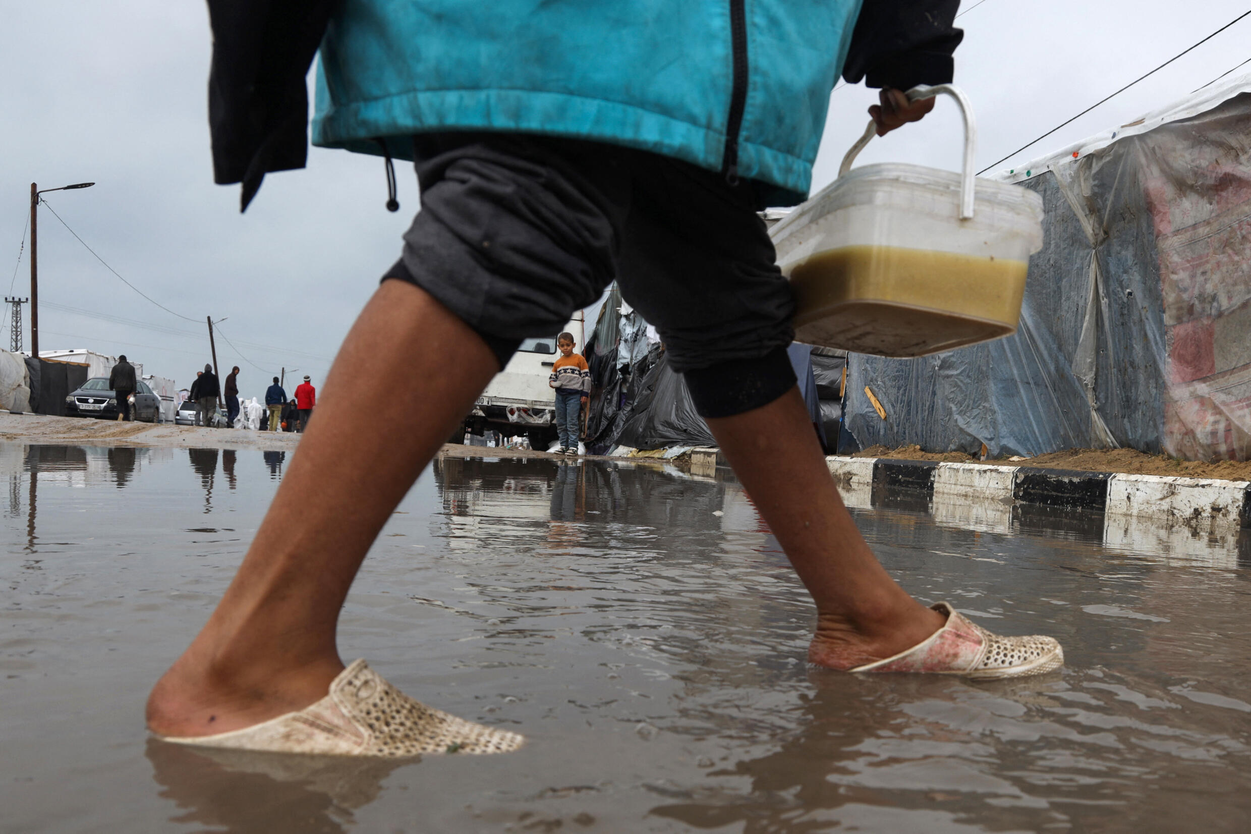 Displaced Palestinians walk through puddles in rainy weather to collect food rations, in a tent camp set up in Rafah, in the southern Gaza Strip, February 2, 2024.