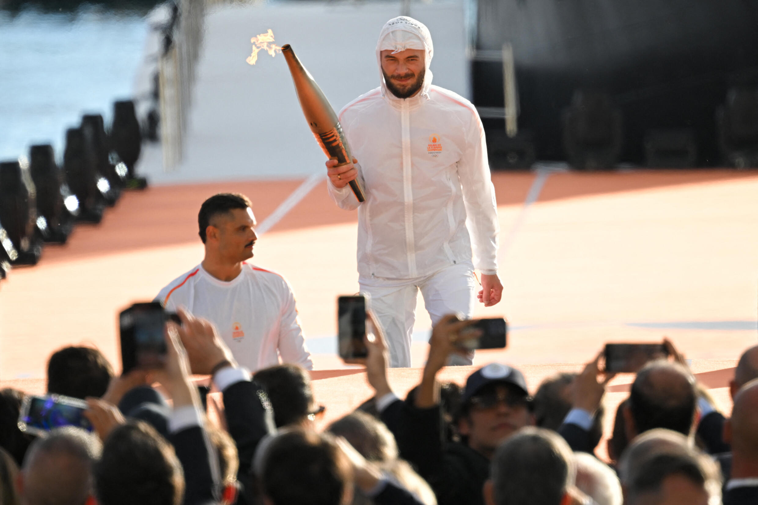 French rapper Julien Mari, aka Jul (center), holds the Olympic flame next to French swimmer Florent Manaudou (left) during the Olympic flame arrival ceremony at the Old Port.  Marseille, in the south-east of France, May 8, 2024.
