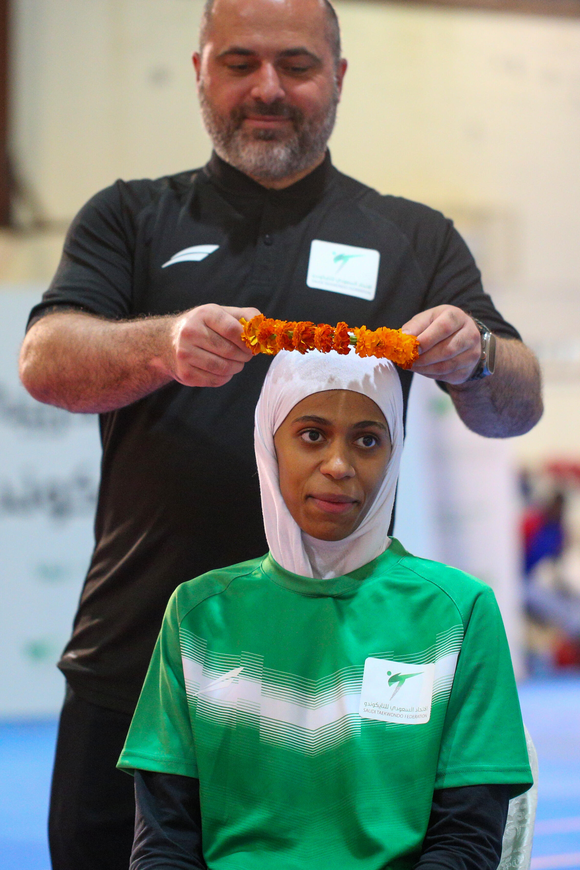 Russian Kurban Bugdaev, coach of the Saudi Olympic taekwondo team, places a laurel wreath on the head of Donia Abu Taleb, who hopes to win a gold medal at the Paris Games, on June 9, 2024 in Abha