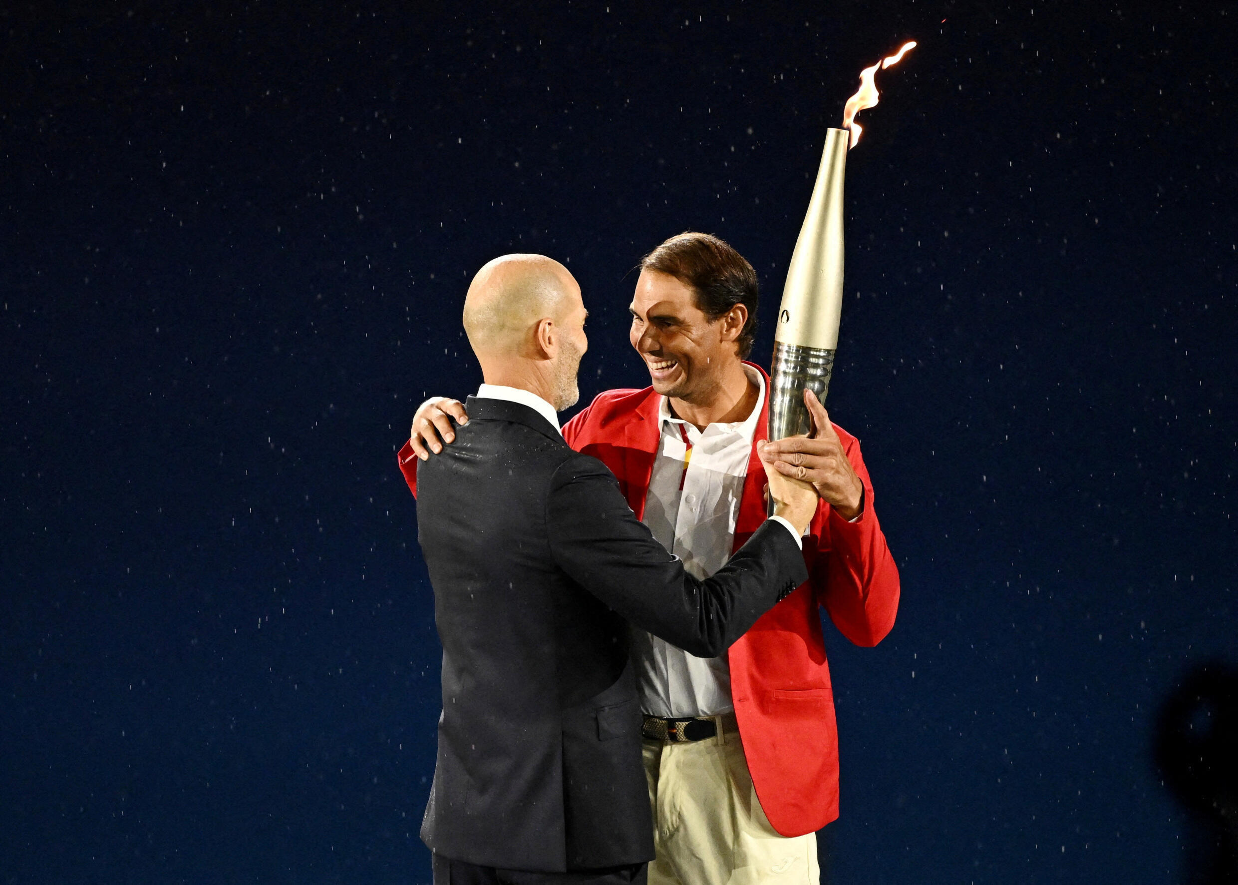 Former footballer Zinedine Zidane passes the Olympic flame to tennis player Rafael Nadal during the opening ceremony of the Paris 2024 Olympic Games on July 26, 2024.
