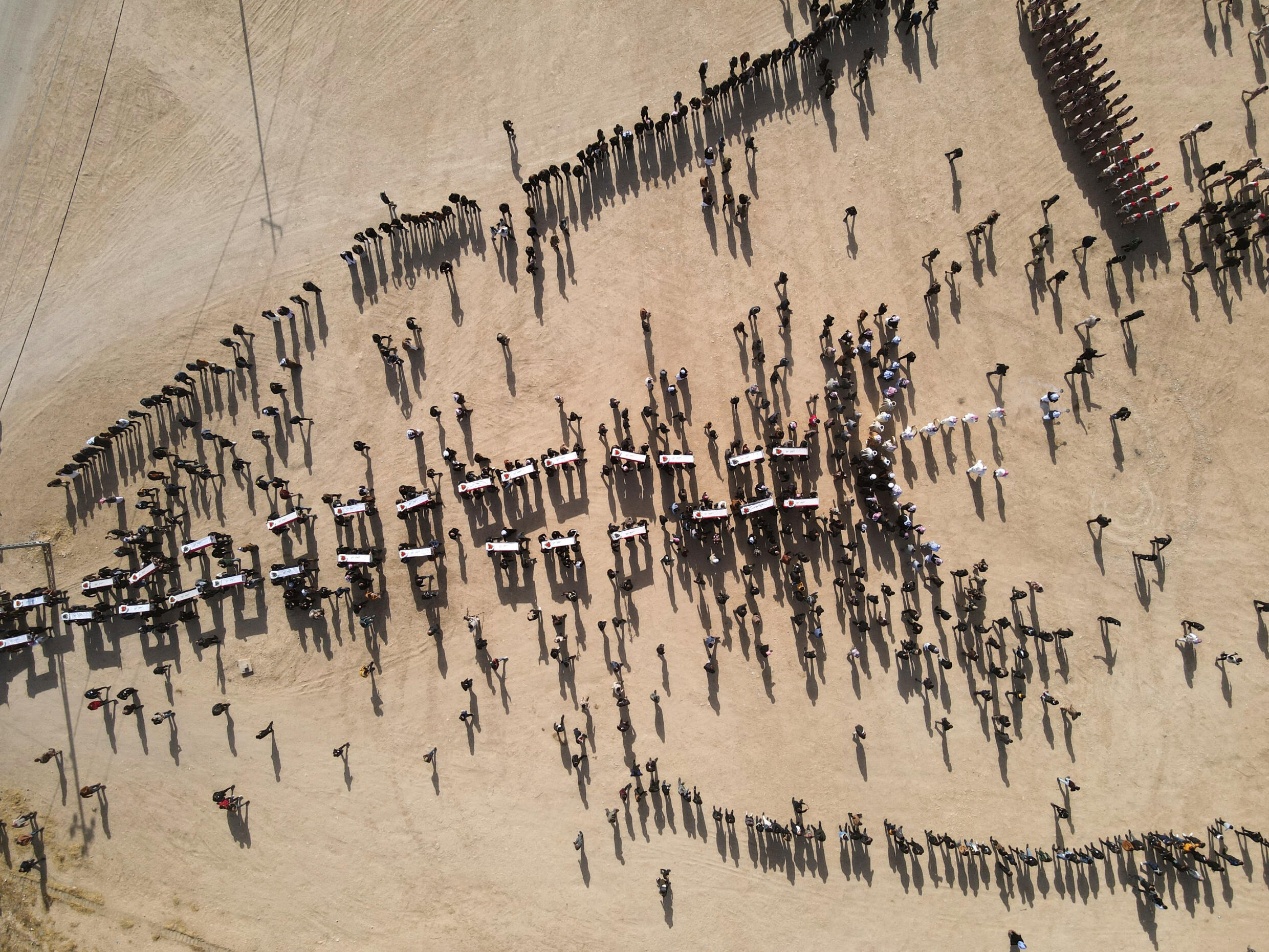 An aerial photo shows mourners carrying coffins during a mass funeral of Yazidi victims of the Islamic State (IS) group whose remains were found in a mass grave, in the village of Kojo in Sinjar district, northern Iraq, December 9, 2021.