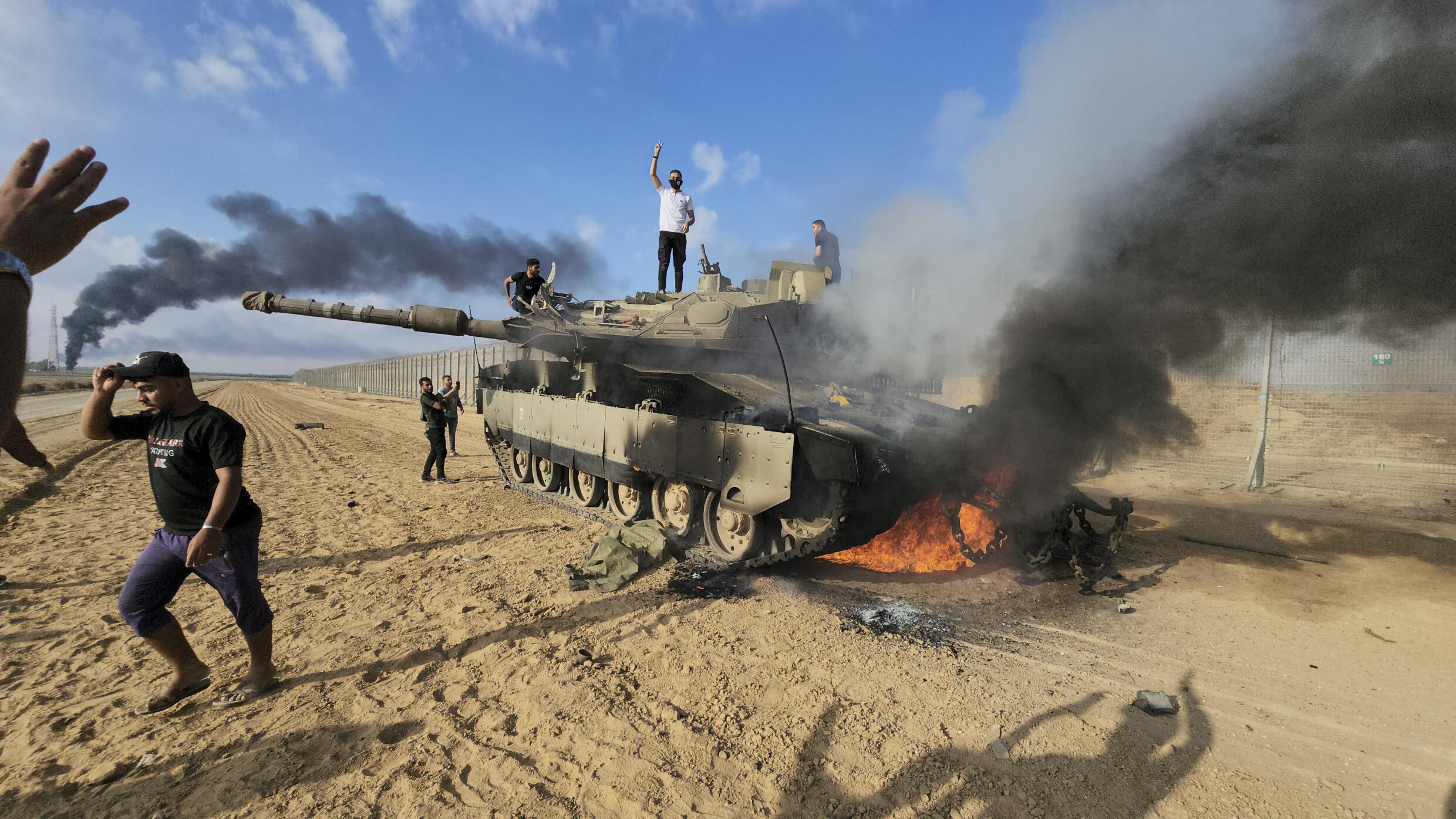 Palestinians in front of a burning Israeli tank near the Gaza Strip fence, east of Khan Younis, Saturday, October 7, 2023.