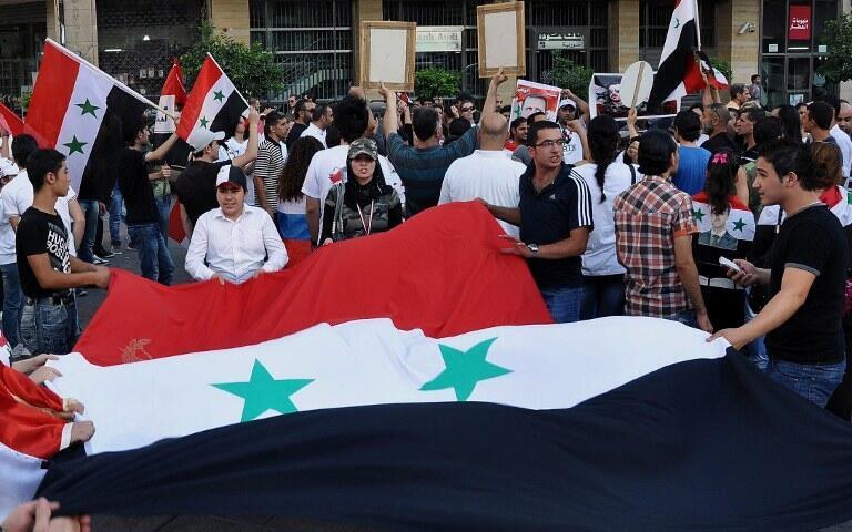 Pro-government Syrians unfurl a Syrian flag in Damascus on July 18, 2012.